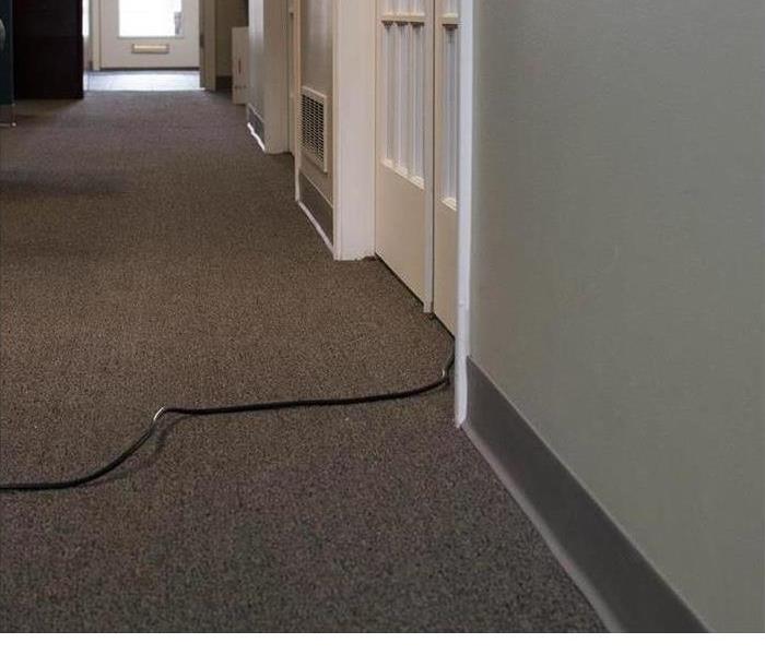 carpet pulled up in a hallway because of damage and a SERVPRO armorer drying the floor 